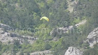 橙色条纹的黄色滑翔伞在灰色大岩石的背景下在美丽的山区飞行