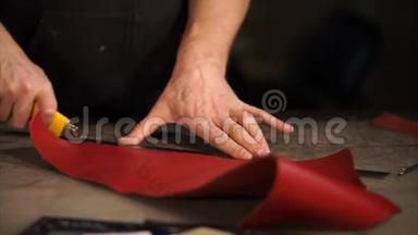 皮匠正在工作室的一张工作桌上剪一条红色油漆的皮