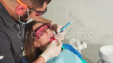 戴眼镜的<strong>牙齿矫正</strong>医生用激光给一个年轻女人美白<strong>牙齿</strong>
