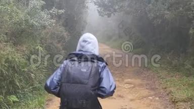 徒步旅行的女人带着背包在热带潮湿的森林里奔跑。 小女孩穿着雨衣在旅途中沿着木小径慢跑