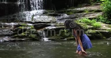 年轻女子站在瀑布附近的河里溅水。 女人微笑着，深深地呼吸着。