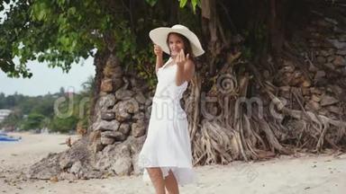 年轻的黑发女人，<strong>头戴</strong>白色的长发，<strong>头戴</strong>帽子，招手跟着她，走在热带海滩上，扔东西