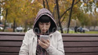 一位身穿连帽衫的年轻女子在秋<strong>季</strong>公园使用智能<strong>手机</strong>。