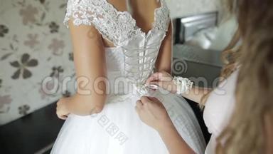 伴娘在婚纱上系蝴蝶结。 新娘为婚礼做准备。 婚纱特写