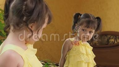 镜子前的小女孩咬着嘴唇。 镜旁一个穿黄色连衣裙的漂亮孩子.. 有尾巴的女孩。