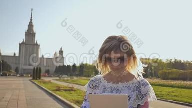 年轻女孩使用平板电脑户外和微笑。 女孩在公园里使用数字平板电脑。 学生<strong>放学</strong>后使用平板电脑