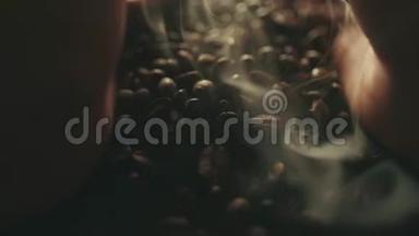 香喷喷的烤咖啡豆从人手里溅出来.. 慢运动中的芳香烟雾和棕色背景