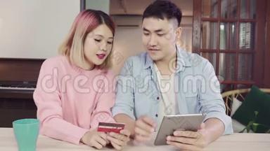 年轻的亚洲家庭夫妇使用平板电脑讨论新闻或做网上购物一起坐在办公桌上周末在家里。