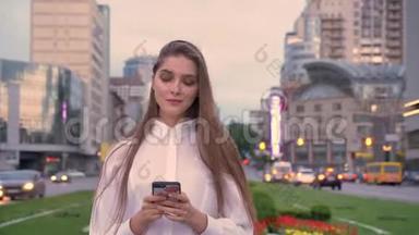 年轻漂亮的女孩正在夏季市中心日落时分的智能手机上输入信息，这是一种沟通观念