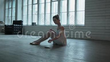 一个坐在地板上的年轻女人拿着一个记号笔，把它们画在鞋子上。 在木地板上漂亮的金发女郎