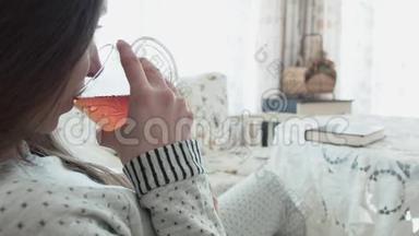 一个甜美的年轻女人正在喝茶，穿着睡衣看书。 一位美丽的年轻女子正在喝茶，吃东西