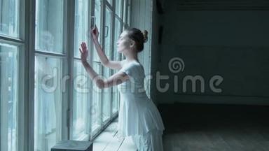 一个年轻的女人穿着白色的连衣裙在窗户附近跳舞，穿着连裤袜在网<strong>眼里</strong>跳舞。 漂亮的金发女郎靠近老大窗户