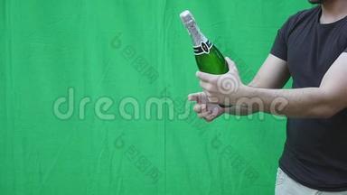 男人`绿色背景上拿着一瓶香槟的手