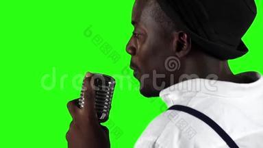 一个年轻的非洲裔美国人从后面的视线接近麦克风在录音室唱歌。 绿色屏幕
