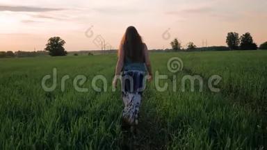 年轻的女孩带着微笑，<strong>直发</strong>，穿着一件长裙，沿着绿色的田野奔跑。 夕阳西下。 慢动作