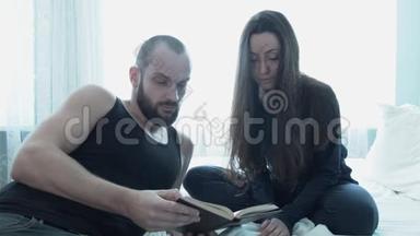 美丽<strong>的夫妻在床上</strong>讨论一本书。 一对年轻快乐<strong>的</strong>知识分子<strong>在床上</strong>讨论这本书。