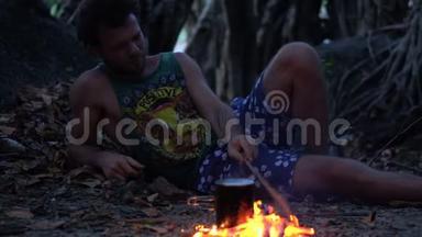 白种人野蛮人在热带森林里燃烧小篝火，在暮色中煮水壶和米饭作为晚餐。
