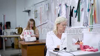 两名妇女从事服装制造。 穿着白色西装的女人坐在<strong>前台</strong>，在现代服装上缝制粉红色的布