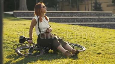 红头发的女人<strong>坐在</strong>自行车上躺在城市公园的草<strong>地上</strong>。 女子自行车公园