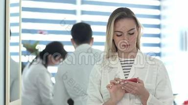 漂亮的护士使用手机，另一个护士清洁<strong>接待处</strong>