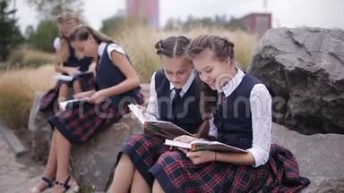 一群穿着相同校服的学生在户外看书时坐着聊天