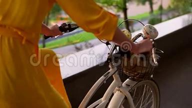 城市自行车的近景`有铃铛、篮子和鲜花的车把。 无法辨认的女人骑着城市自行车