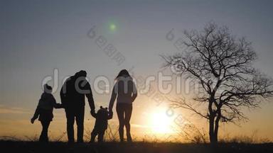 日落时，幸福的家庭在一棵<strong>大树</strong>附近的草地上散步的<strong>剪影</strong>。