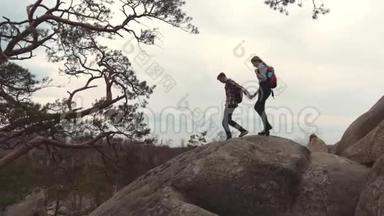 一对年轻情侣拿着背包，手牵着手，沿着高高的石头山爬山。 旅游
