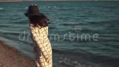 年轻女子在水边享受一个温暖的秋天下午。 穿着<strong>秋装</strong>戴着帽子的女孩在日落时沿着海岸散步