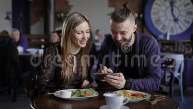 快乐的一对夫妇一起吃午饭，看智能<strong>手机</strong>。 男人和女人用<strong>数码</strong>小玩意笑照片