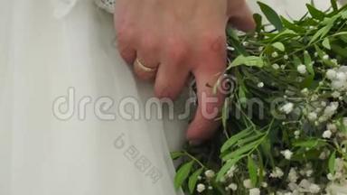 新娘手里的婚礼花束`不错。 剪辑。 未婚妻穿着一件漂亮的白色连衣裙，捧着一束美丽的婚礼花
