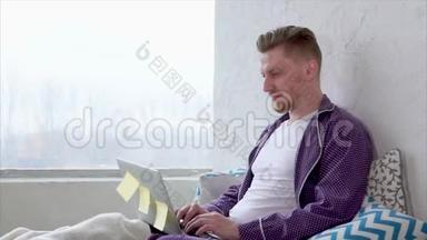 有笔记本电脑的人坐在床上。 早上在家上网。