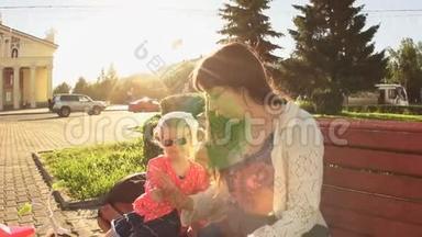 日落时分，母亲和女儿正坐在靠近马路的广场上的长凳上。