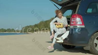 一个女人坐在海边的敞篷后备箱里的四弦琴上玩耍