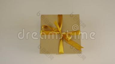 白种人的手从白色的桌子上拿走棕色的礼盒。 带蝴蝶结的金色丝带。 一个礼品盒。 概念庆祝活动