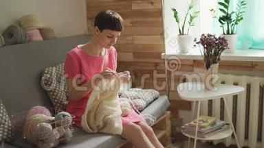 年轻女子在舒适的房间里的沙发上编织<strong>羊毛</strong>衫。 女人编织<strong>羊毛</strong>