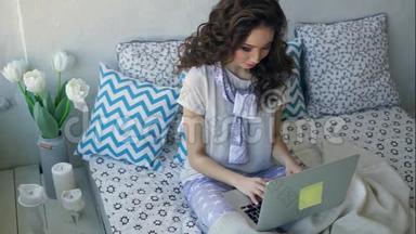漂亮的女人坐在舒适的房间里的床上，用笔记本<strong>电脑打字</strong>。