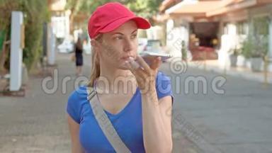 戴着红帽子的漂亮女游客用智能手机在街上走来走去，和朋友聊天