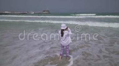 年轻女孩在迪拜海滩上的智能手机上拍摄波斯湾海浪的照片
