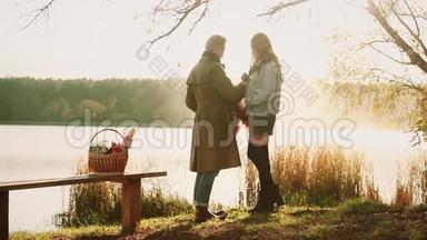 秋天的一对。 美丽的一对穿着温暖衣服的夫妇站在湖边，那里映着秋天的天空，褪色了，野餐了
