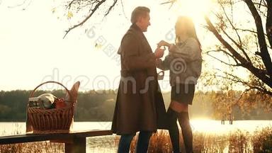 秋天的一对。 美丽的一对穿着温暖衣服的夫妇站在湖边，那里映着秋天的天空，褪色了，野餐了