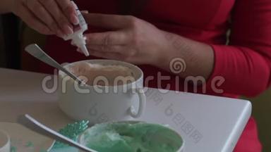 一个女人从一管奶油奶酪中加入一滴食用色素。 着色奶油，以润滑蛋糕。