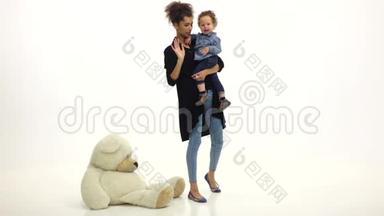 非裔美国人妈妈把婴儿放在地上，玩具熊放在地上。 白色背景。 慢动作