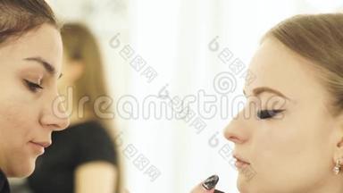 女人化妆师用化妆刷来化妆眼睛美容模特。 把脸贴紧做化妆脸