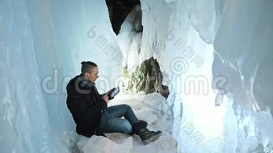 人类坐在冰<strong>洞</strong>里的平板电<strong>脑</strong>上。 围绕着神秘美丽的冰窟.. 用户在