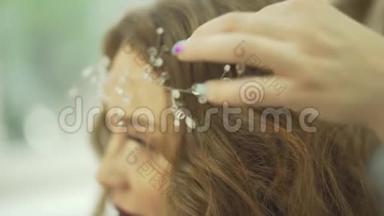 专业发型师沙龙理发师在金发波浪型女模特头上固定珍珠皇冠珠宝首饰上的饰物