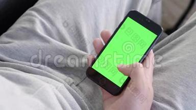 男人在家坐在沙发上，使用带有绿色<strong>模拟</strong>屏幕的智能<strong>手机</strong>
