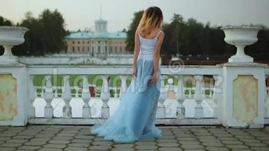 漂亮的瘦女孩穿着白色和蓝色的裙子，站在靠近白色石头<strong>栏</strong>杆的把手，在裙子<strong>底</strong>部摆姿势。