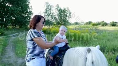 一个带着孩子的女人在田野里走来走去，一个婴儿坐在小马上，妈妈抱着孩子。 快乐的家庭假期