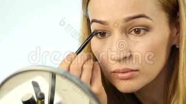 美丽的女人在小镜子前<strong>画眉</strong>毛，用化妆刷做日常化妆。 慢动作